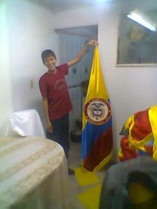 Elaboración venta y fabrica de banderas julio chico joven sosteniendo banderas de Colombia para interior en tela satín razo o pesado
